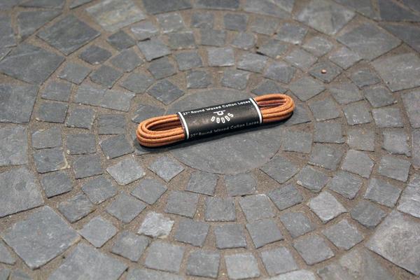 A pair of Alden Madison Laces - Shoe Lace Guarded Goods, 27 inches long, neatly coiled and wrapped with a black label, rests on a circular stone tiled surface.