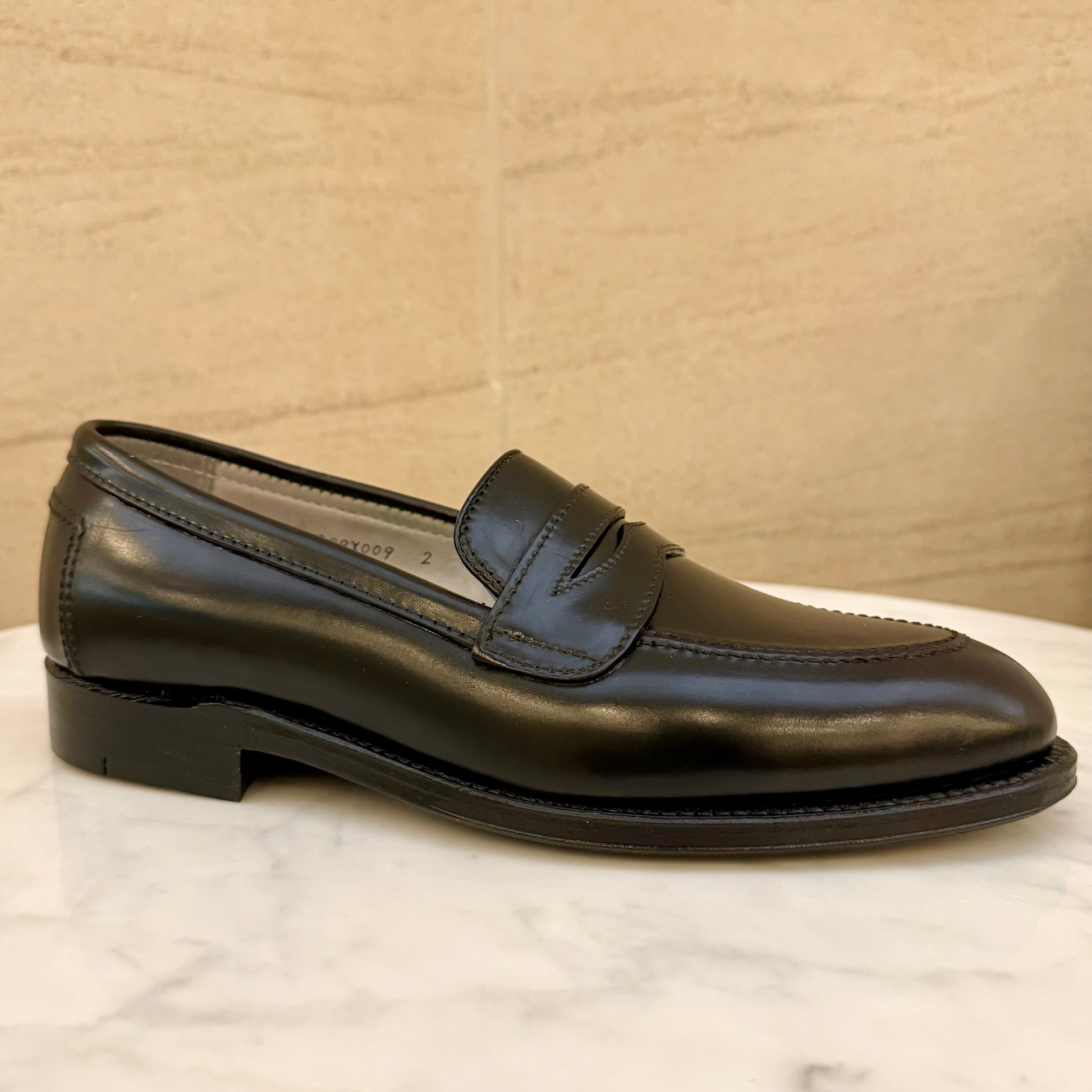 The ALDEN SHOES 5751 - High Vamp Loafer in Black Shell, featuring a low heel and sleek Aberdeen Last design, is displayed on a white marble surface with a beige background.