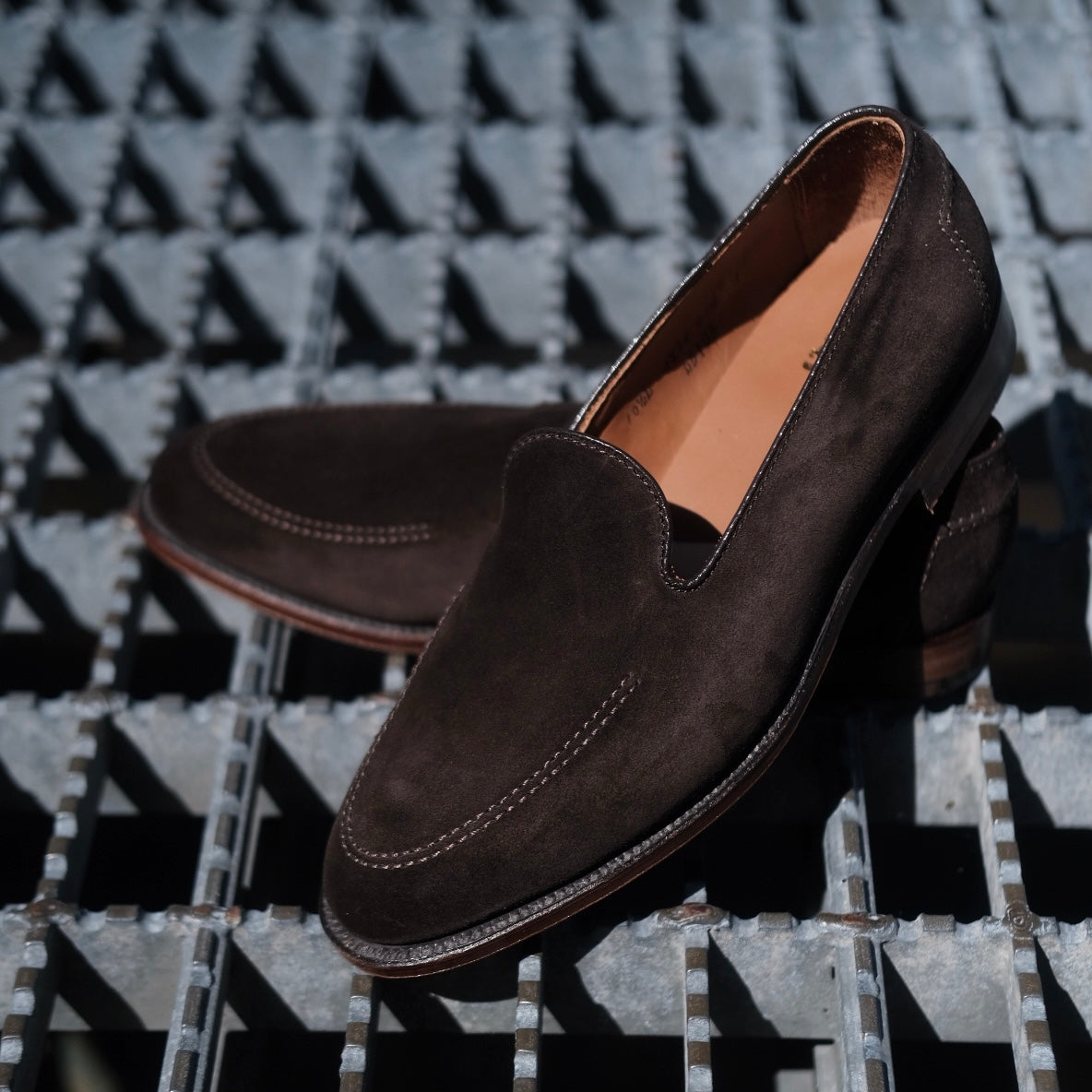 A pair of ALDEN SHOES D5105 - Vanderbilt in Dark Brown Suede, featuring visible stitching and a flex leather sole, displayed on a metal grid surface.