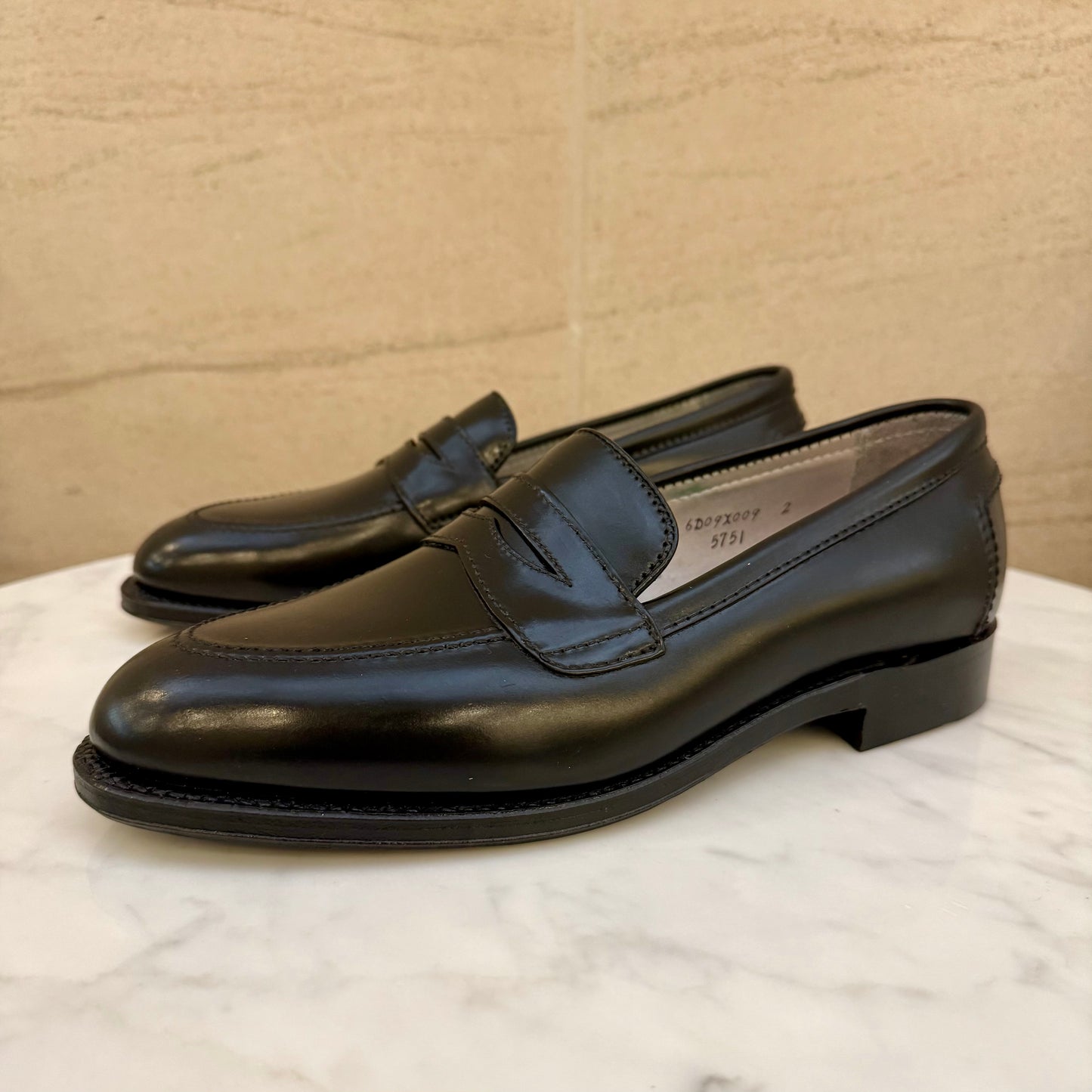 The ALDEN SHOES 5751 - High Vamp Loafer in Black Shell is shown on a white marble surface with a beige stone background.