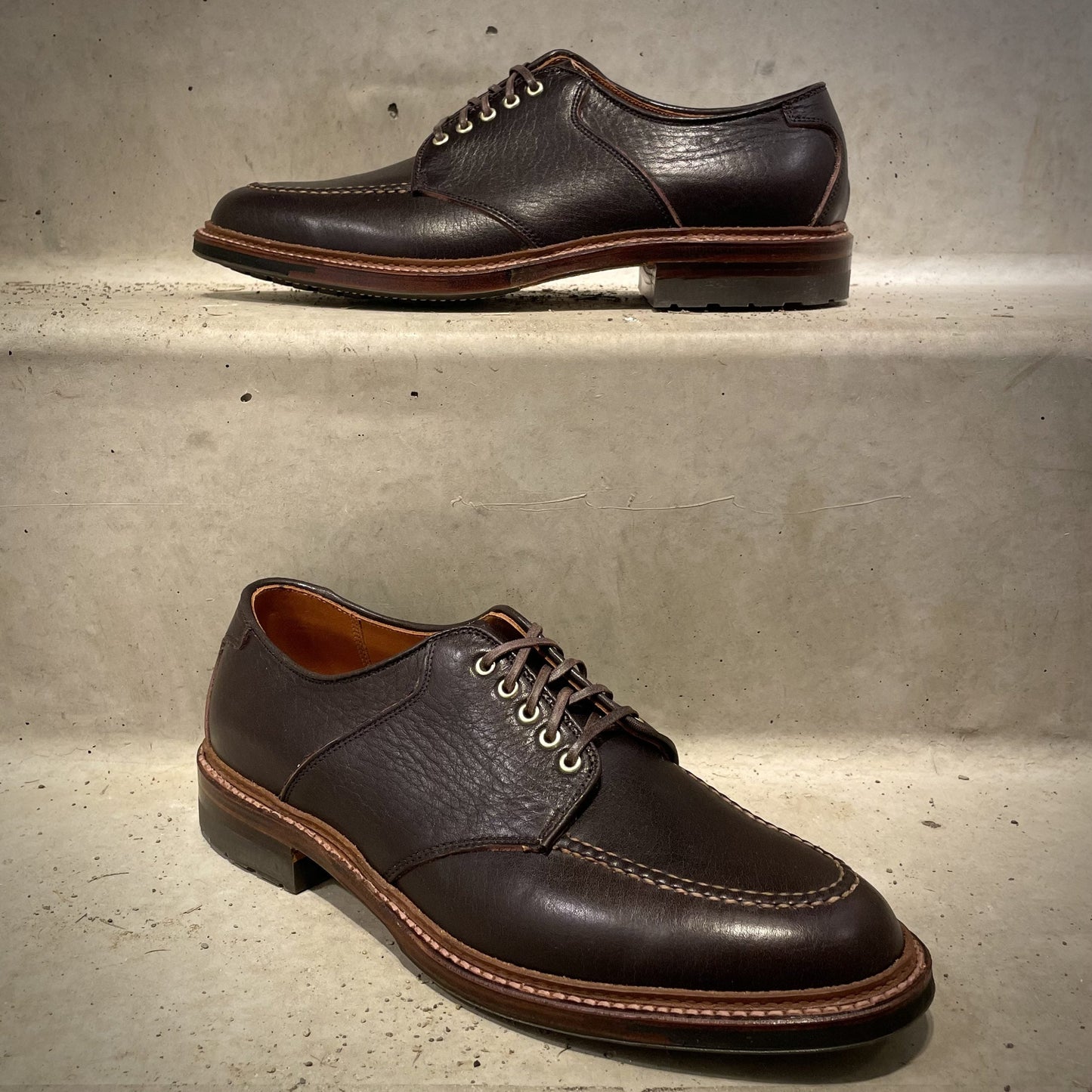 Alden Madisons D1613C The Belmont Saddle Blucher Lux Arabica Calf dress shoes feature dark brown calfskin leather with light brown soles and stitching, displayed on a light gray surface with one shoe elevated above the other.