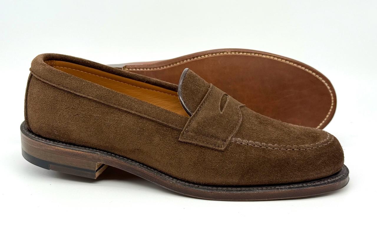 The Alden Madison 6175F - Penny Loafer in Humus Suede features stitching details, is crafted on the Van Last, and comes with Flex Oiled Leather soles and a low stacked heel. One shoe is upright while the other shows its sole.