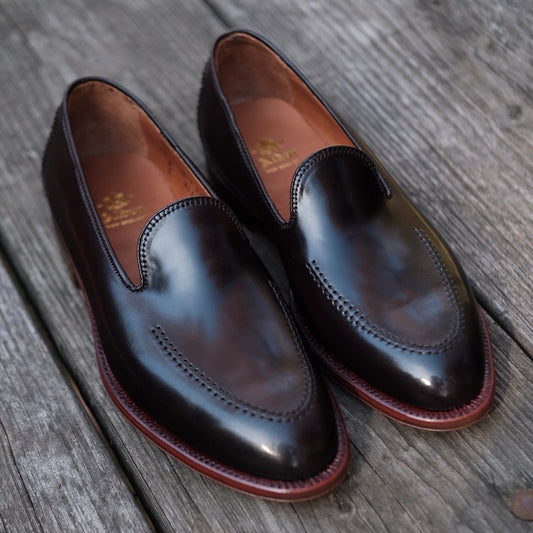 The Alden Madison Vanderbilt Slip On (D1118) in Color 8 Shell, designed on the Aberdeen Last with sleek stitching and a polished finish, sits on a weathered wooden surface.