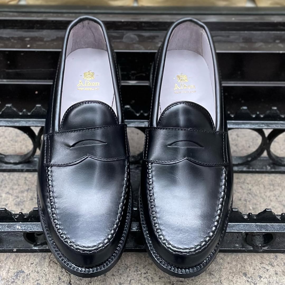Alden Madison 987 - Leisure Hand Sewn Black Shell Cordovan penny loafers with stitching details are displayed side by side on stone, showcasing the gold Alden logo insole and a durable Single Oak Leather Outsole.