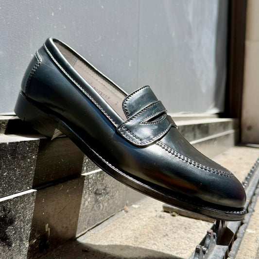 The ALDEN SHOES 5751 High Vamp Loafer in Black Shell Cordovan, crafted on the elegant Aberdeen Last, is shown outdoors on a stone step with sunlight highlighting its polished finish and intricate stitching.