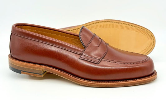 Alden Madison’s 9826 - Penny Loafer in Walnut Michigan Calf, featuring smooth brown leather and a light tan Flex Oiled Leather Sole, is displayed on a white background with one shoe upright and the other showing the sole.