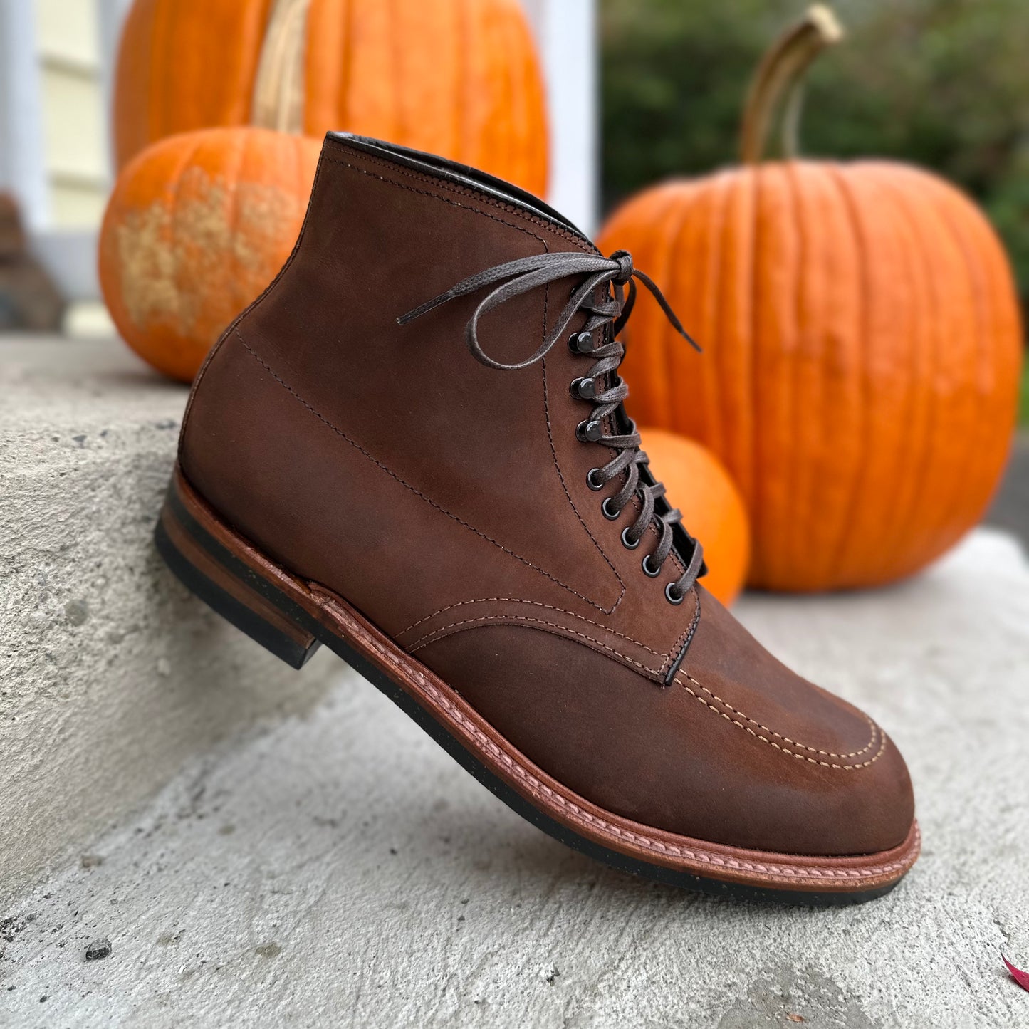 An Alden Madison D2909H - Indy Boot in Tobacco Smooth Chamois sits on a stone step amidst pumpkins, creating a cozy autumn atmosphere.
