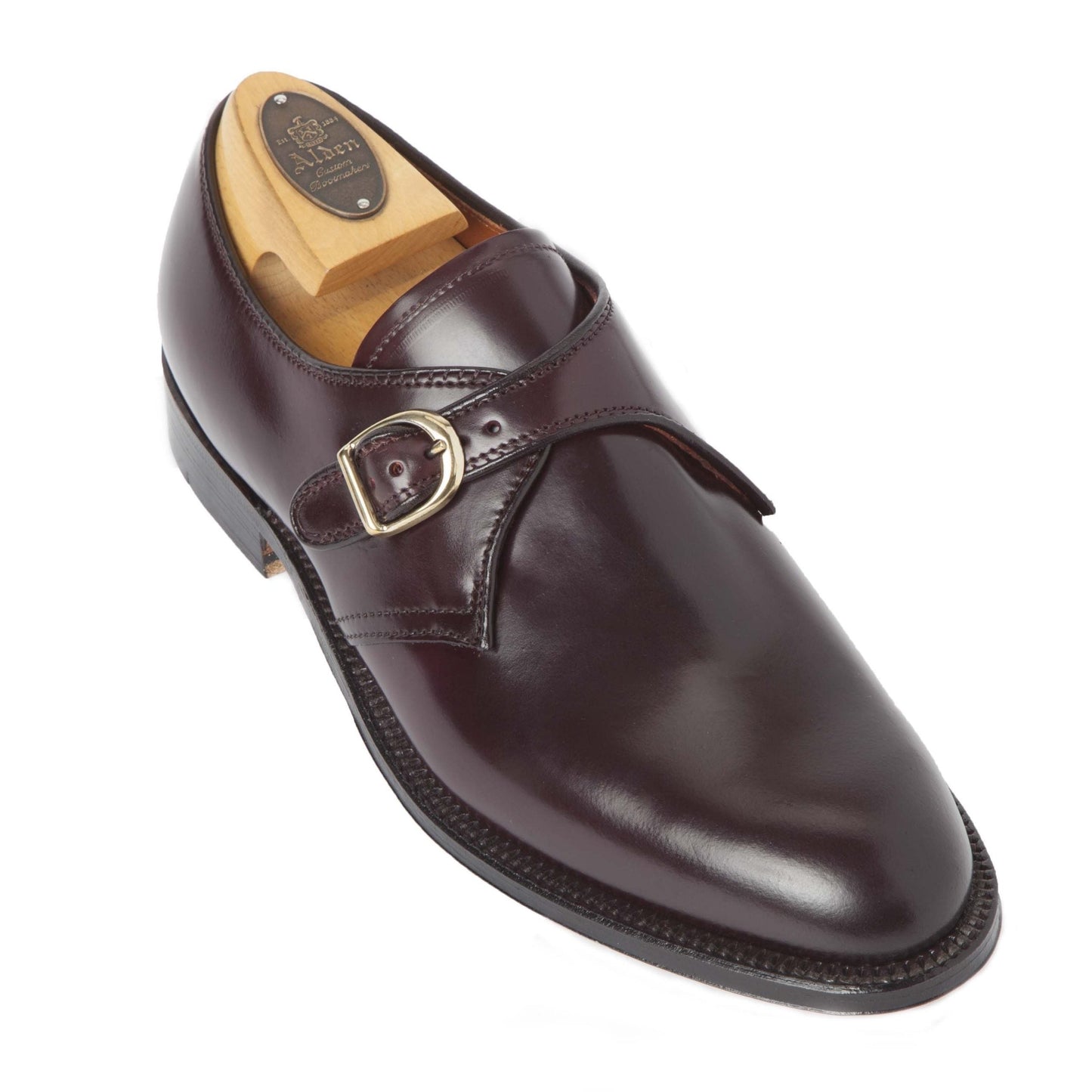 The Alden Madison 954 - Monk Strap Color 8 Shell Cordovan is a dark brown polished leather dress shoe on the Aberdeen Last with a silver buckle and visible branding on the heel, featuring a wooden shoe tree and black sole. Its elegantly angled on a white background.