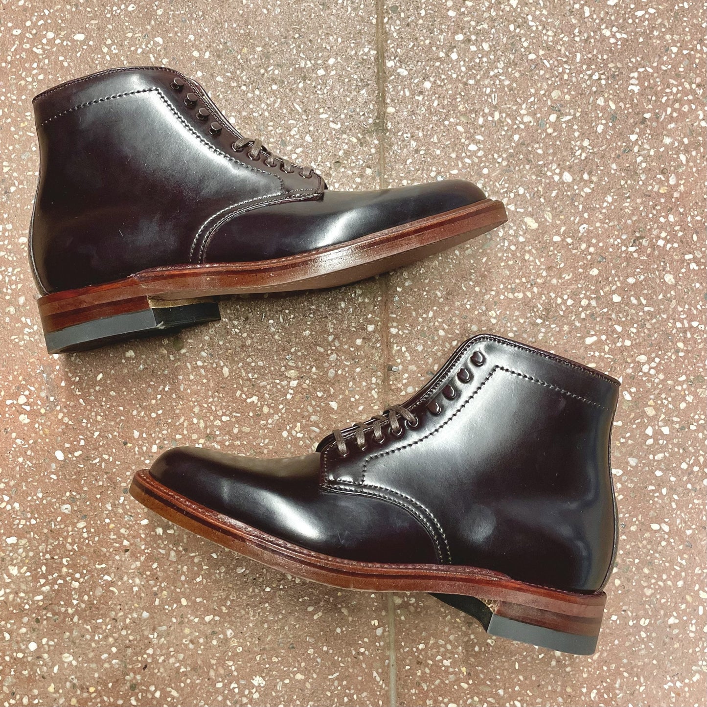 Two polished, dark burgundy Alden Madison D1854H - Plain Toe Boots in Color 8 Shell are placed side by side on a speckled brown tile floor, displaying their outer sides and distinctive wooden Neocork soles crafted with the classic Barrie Last.