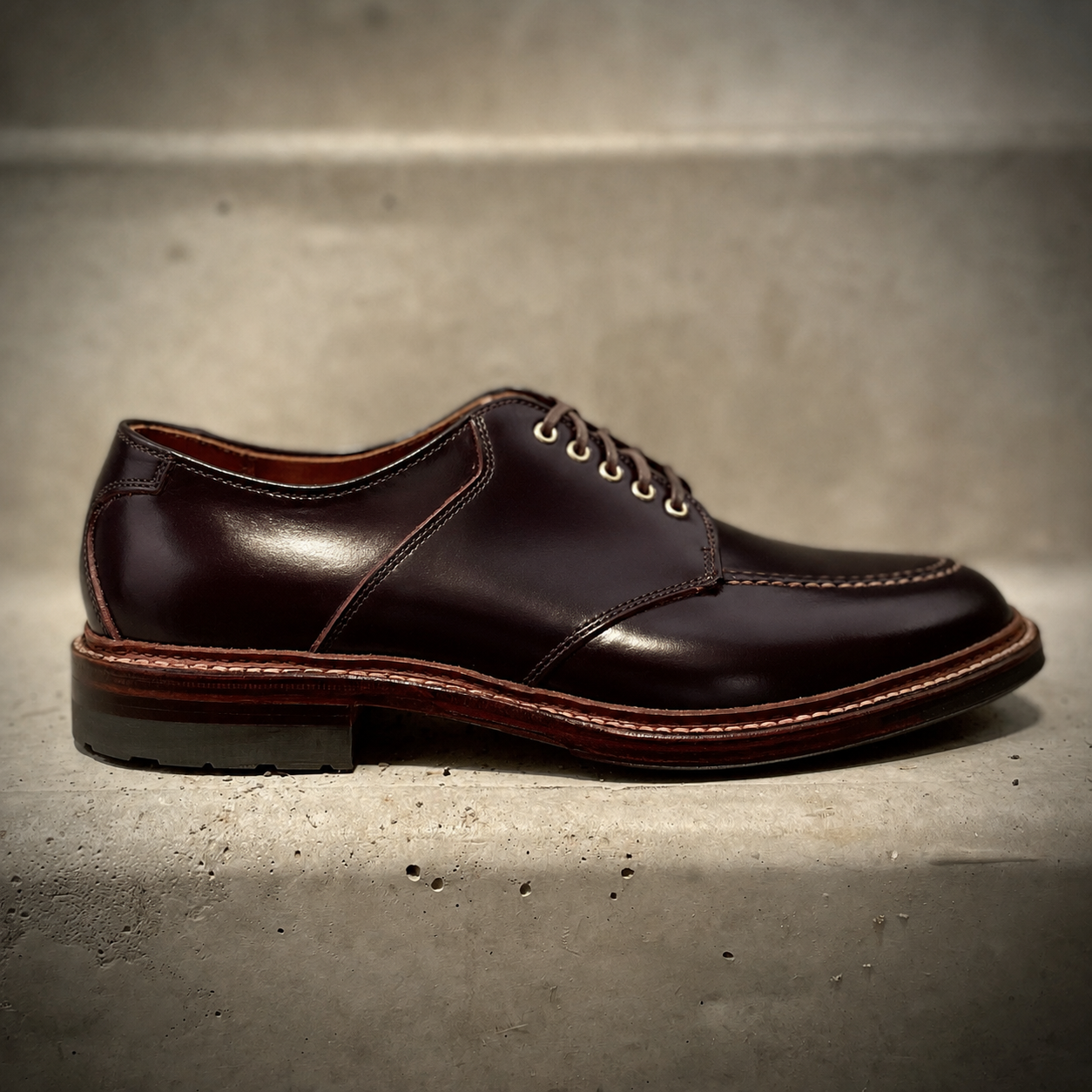The ALDEN SHOES D5617 - Saddle Blucher in Color 8 Shell features dark brown Shell Cordovan leather, stitching details, and a wooden sole, showcased on a concrete surface.