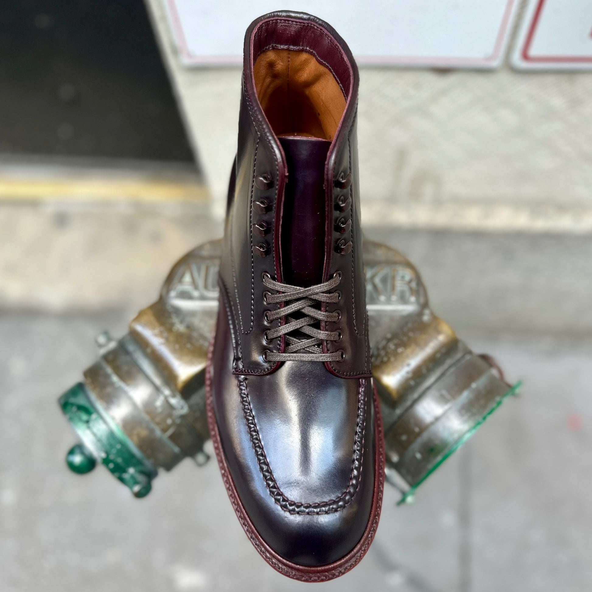 A single Alden Madison D2936H - Color 8 Shell Indy Boot, crafted from rich dark brown Shell Cordovan and featuring intricate stitching, is displayed atop a metal fire hydrant on a city sidewalk, highlighting its Double waterlock sole and timeless Trubalance last.