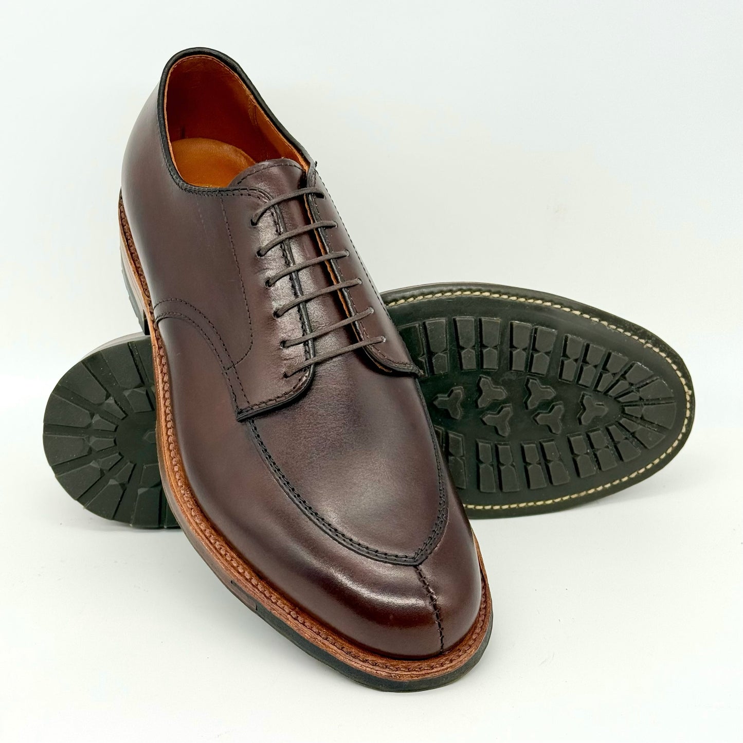 The ALDEN SHOES D6629C Brown Calf V Tip Blucher features detailed stitching, laces, a moc toe design, and a rugged black commando sole. One shoe stands upright while the other lies on its side to show the textured sole.