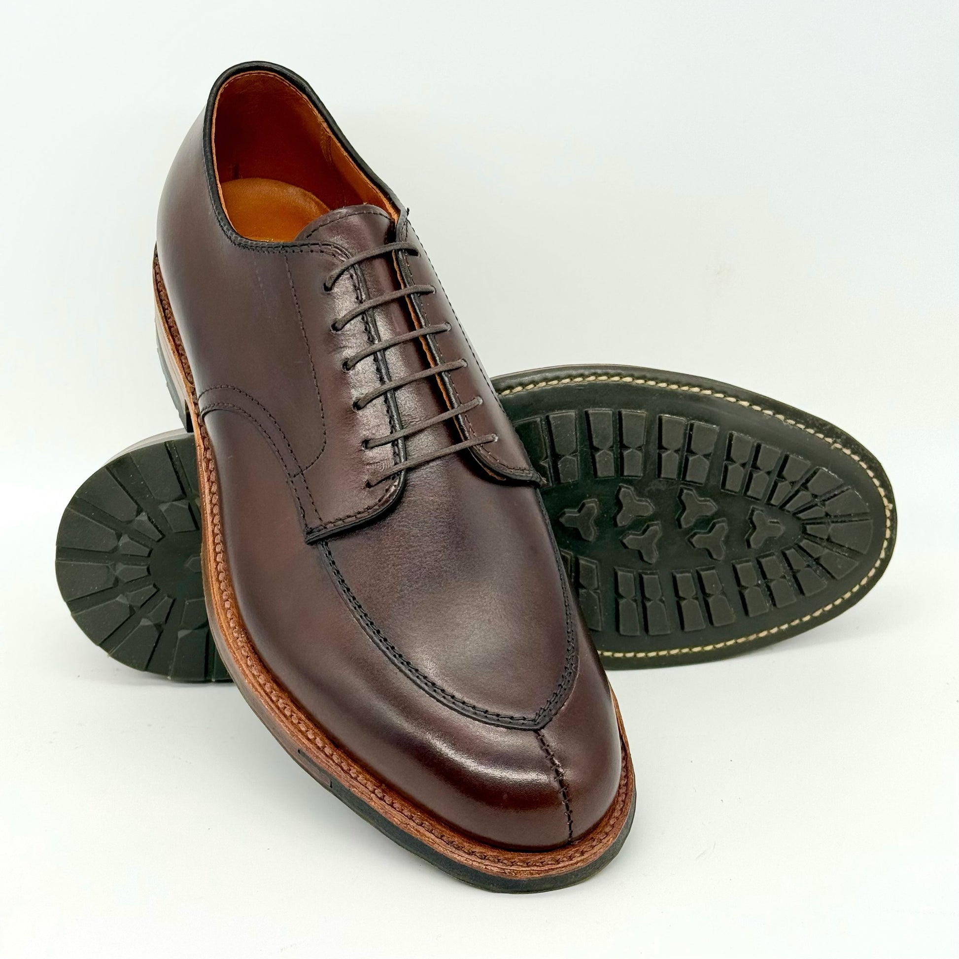 The ALDEN SHOES D6629C Brown Calf V Tip Blucher features detailed stitching, laces, a moc toe design, and a rugged black commando sole. One shoe stands upright while the other lies on its side to show the textured sole.