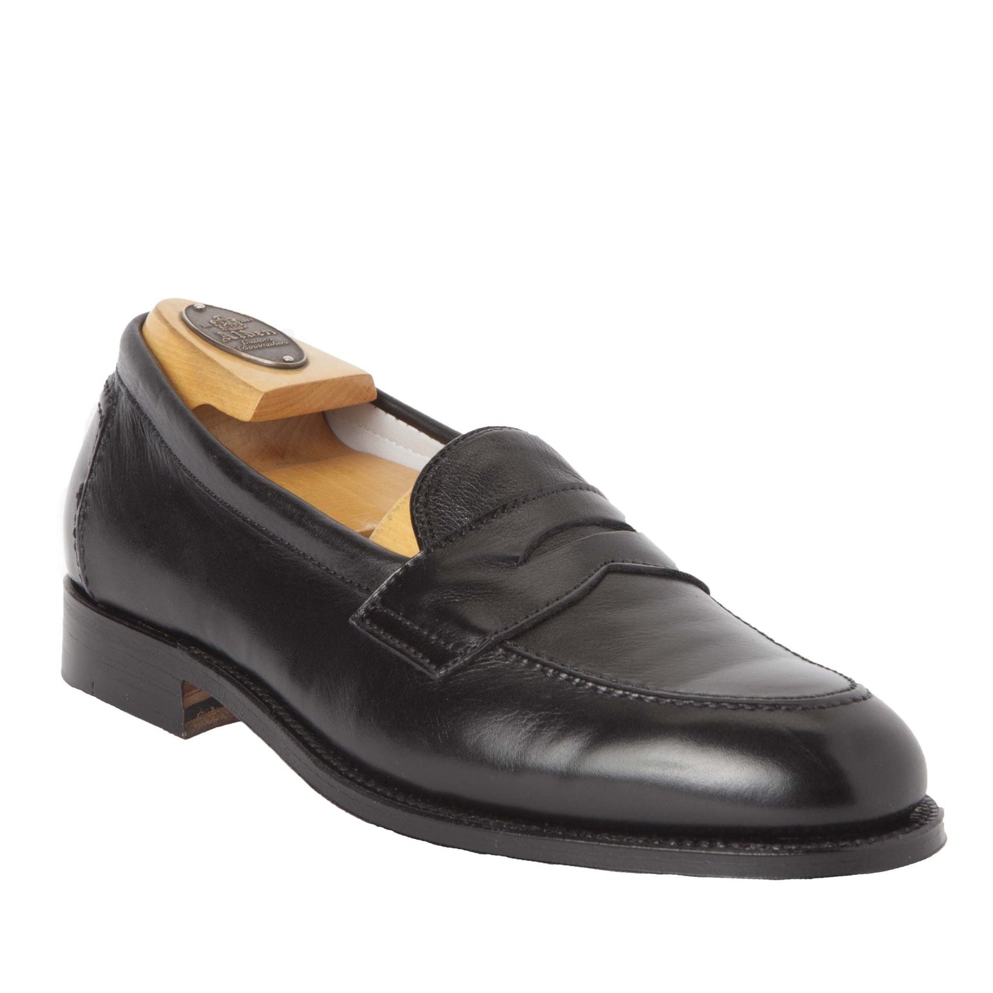 The Alden 9695F Flex Penny Loafer in Black Calfskin features a sleek design with a polished finish, classic penny strap, wooden shoe tree for support, low heel on the Copley Last, and a stitched Flex Leather Sole showcasing traditional craftsmanship.