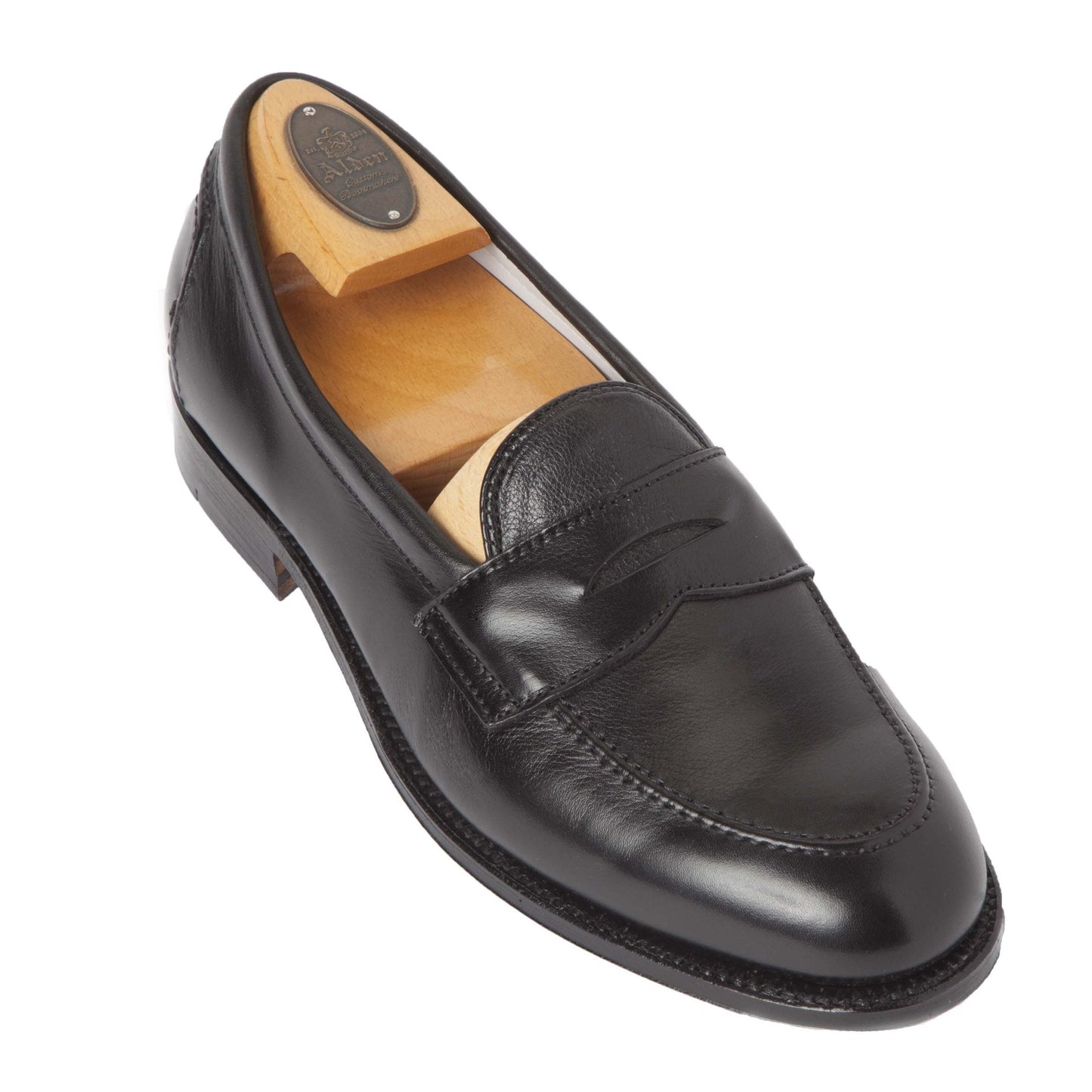 The Alden 9695F - Flex Penny Loafer in Black Calfskin, crafted on the Copley Last with a curved toe design, includes a wooden shoe tree to maintain shape. Its Flex Leather Sole and heel exemplify fine craftsmanship.