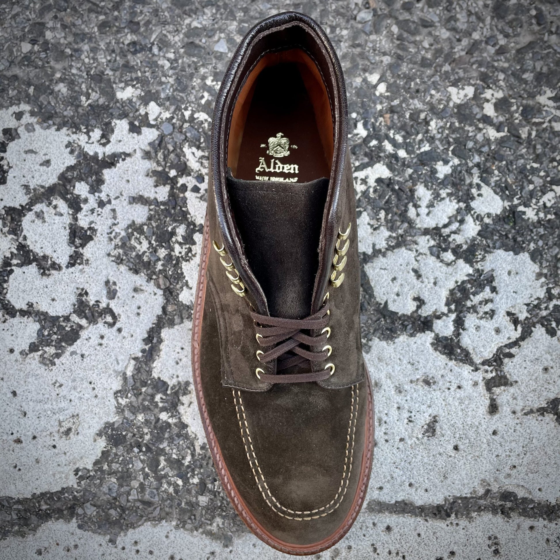 A single D0938H - Duncan Indy Boot in Loden Suede, branded Alden Madison on the insole and laced with dark brown strings, crafted on the Truebalance Last, is positioned on a textured, cracked concrete surface.