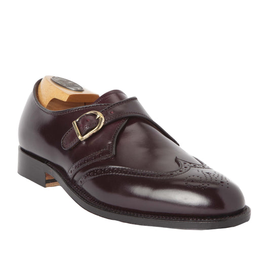 The Alden Madison 1671 - Wing Tip Monk Strap in Color 8 Shell Cordovan showcases a dark brown leather shoe with a decorative buckle and brogue detailing on the toe. It includes a wooden shoe tree and sits elegantly on a white background.