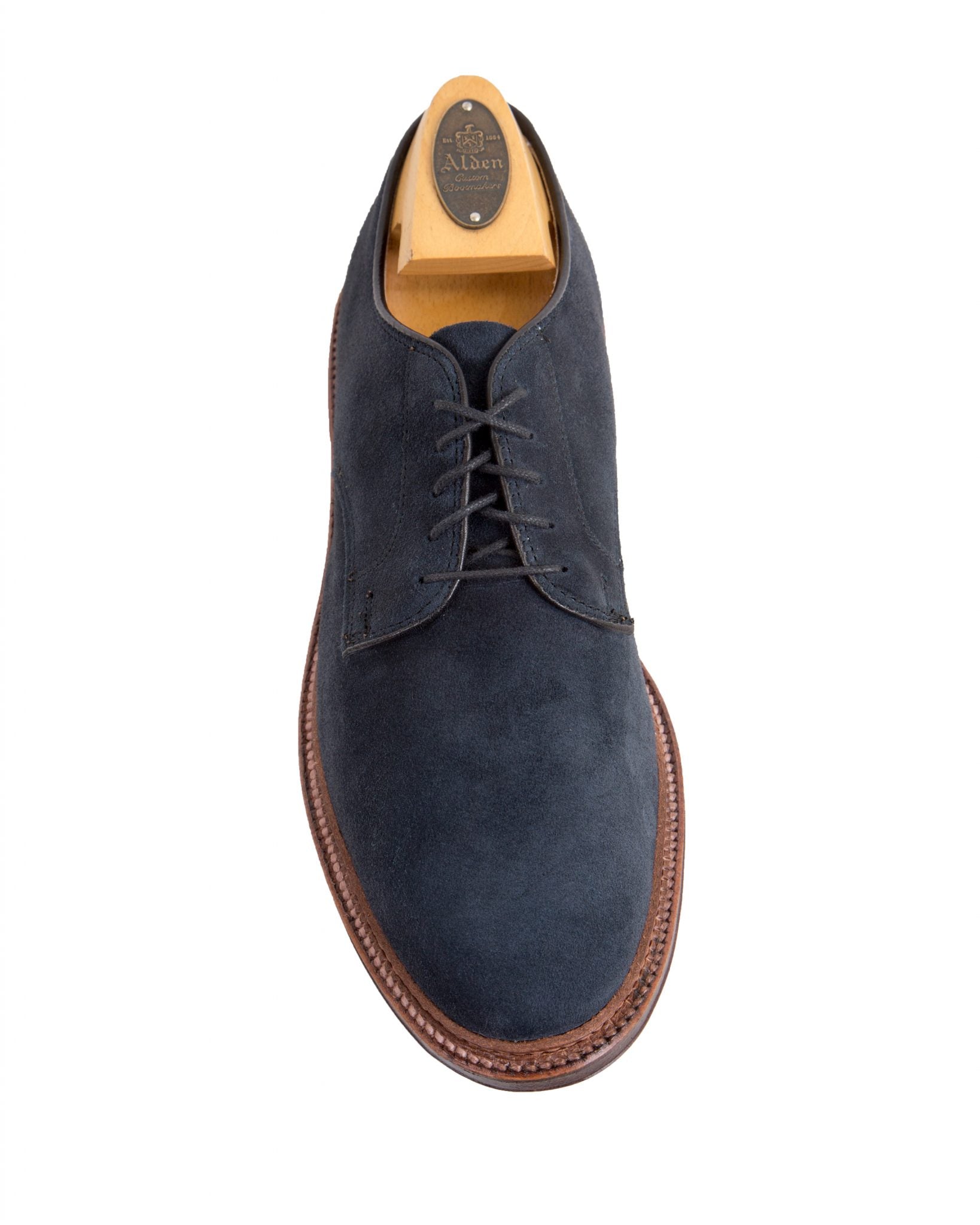 The Alden Madison 29331F Unlined Plain Toe Blucher in blue suede features black laces, a storm welt, and a brown flex leather sole with edge stitching. It includes a branded wooden shoe tree for added elegance and durability.