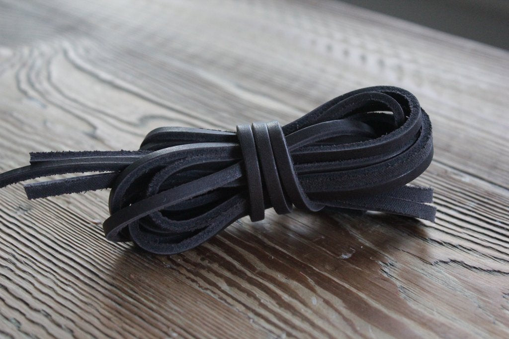 A bundle of Alden Madison Rawhide Laces in Black, cut to size, rests on a textured brown wooden surface.