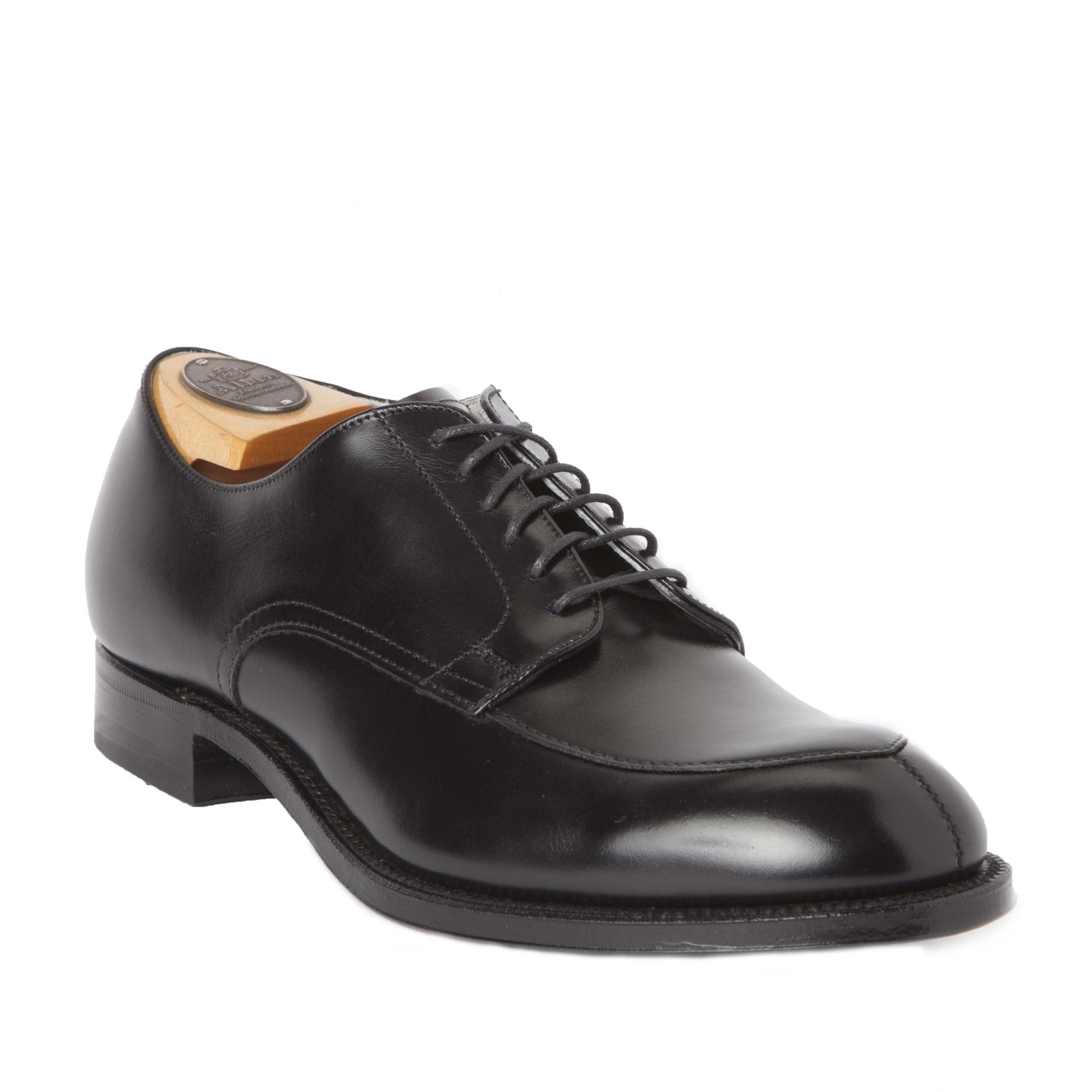 The Alden Madison 539 - Modified V-Tip in Black Calfskin is a polished, professionally crafted dress shoe. Featuring a smooth finish, wide toebox, and sturdy sole, it includes laces and a wooden shoe tree. Positioned at an angle on a white background, the shiny shoe exudes timeless elegance.