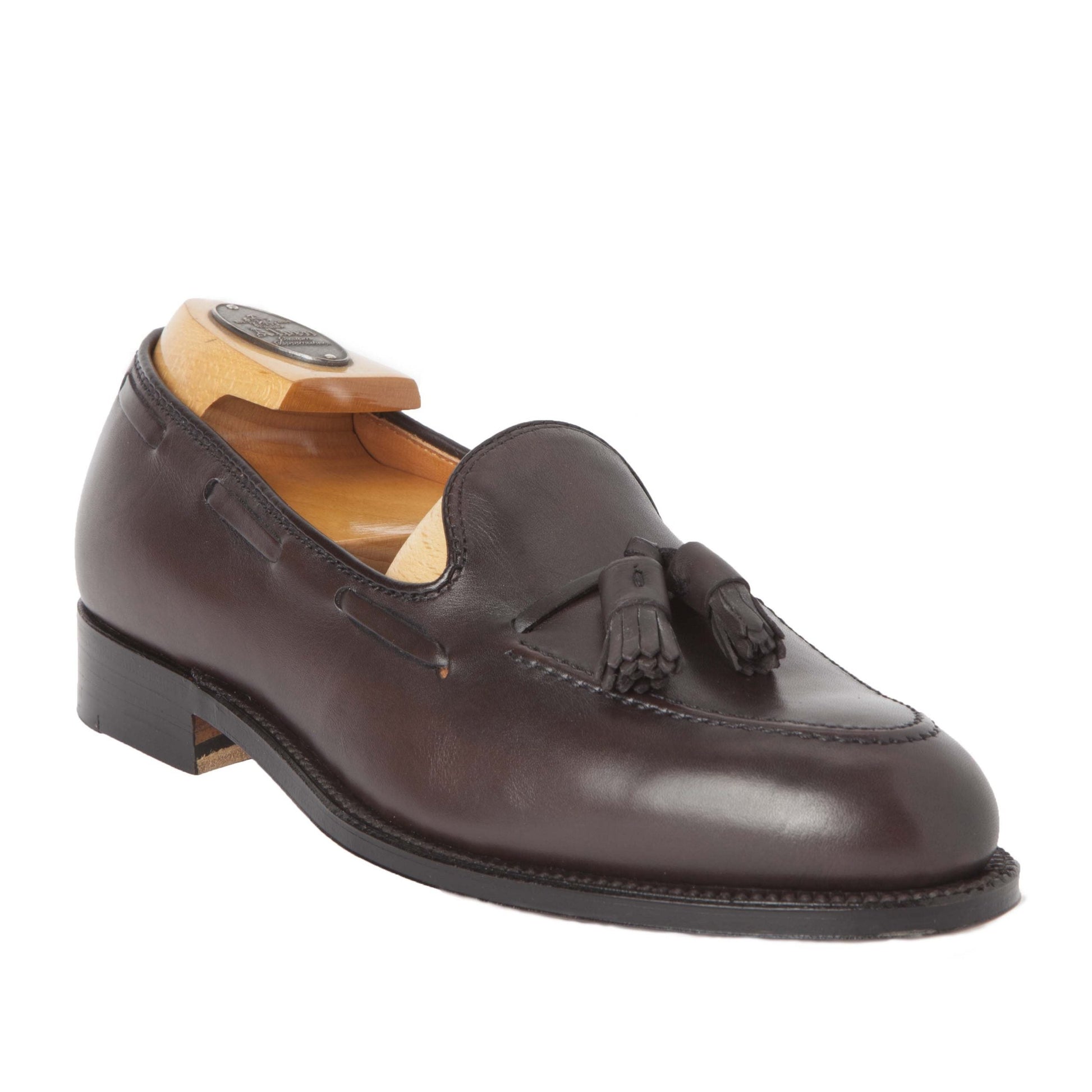 The Alden Madison 561 Tassel Loafer in brown calfskin features a dark brown leather with tassels, crafted on the Aberdeen Last. It has a smooth finish and sits on a low black heel, complemented by a wooden shoe tree for impeccable elegance.