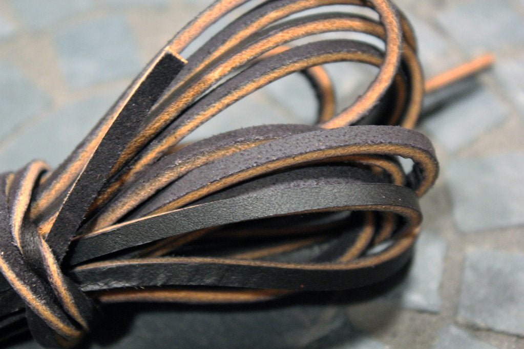 Close-up of several thin, dark brown Alden Madison Laces – Rawhide Laces in Brown/Tan, cut to size and looped with textured surfaces and raw edges, set against a blurred tiled background.