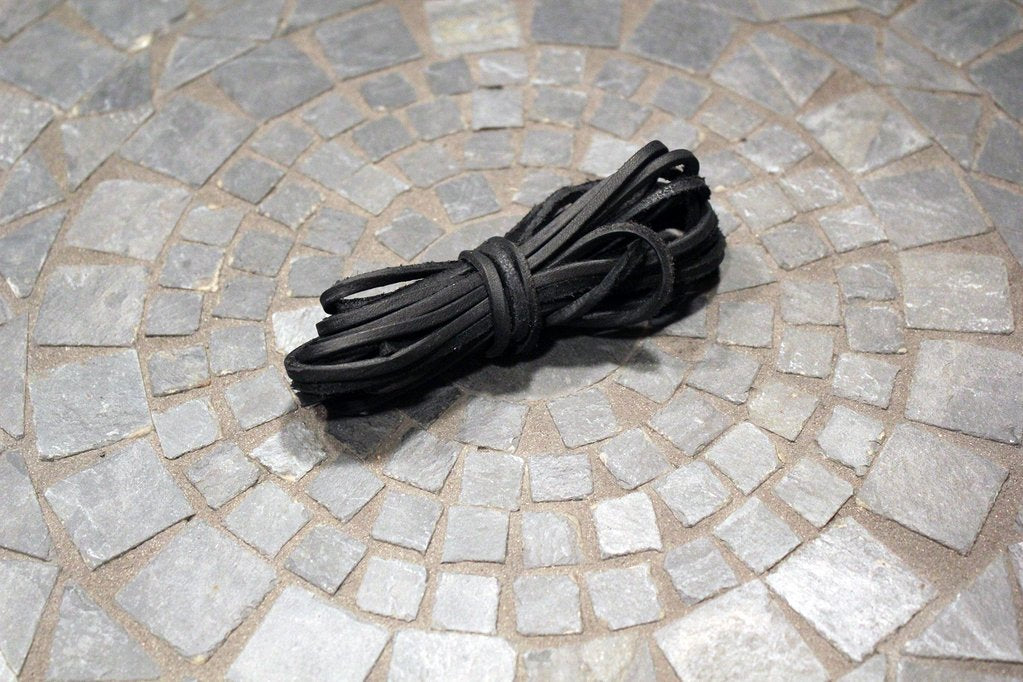 Aldem Madison's black Rawhide Laces rest on a circular stone tile in shades of gray—ideal for 74-inch or cut-to-size needs.