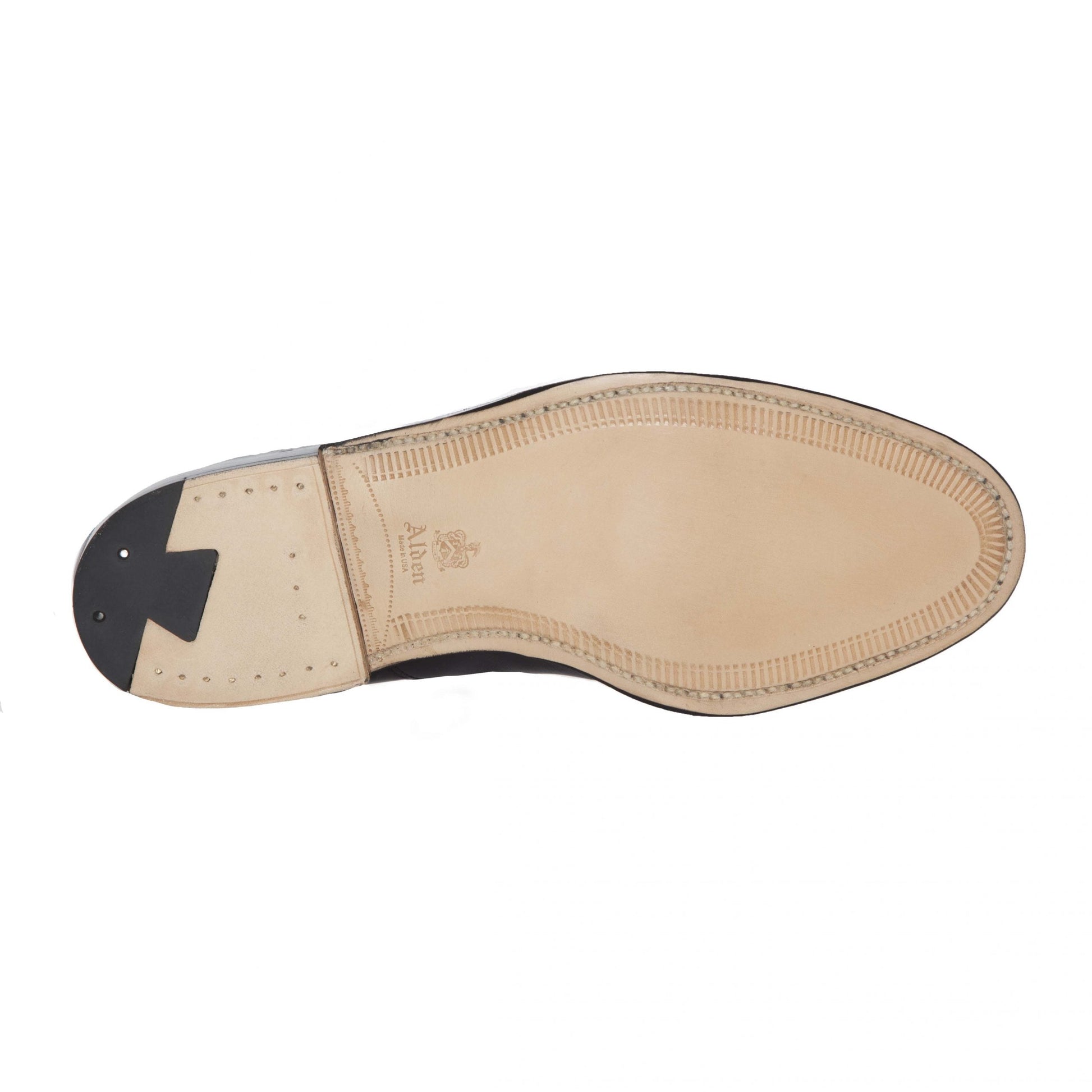 The image displays the sole of a 920 - Cap Toe Bal in Brown Calfskin by Alden Madison, featuring smooth brown calfskin, a black heel with a triangular design and two metal studs, outlined subtly with stitching on an elegantly styled Hampton Last.