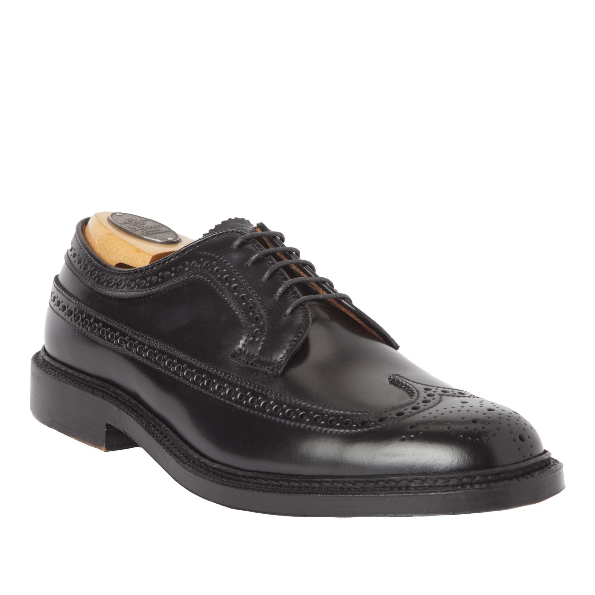 The Alden Madison 9751 - Long Wing Blucher in Black Shell Cordovan is a polished black leather brogue on the Barrie Last, featuring intricate perforations, laces, and a Double Oak Leather Sole. Displayed with a wooden shoe tree to preserve its shape.