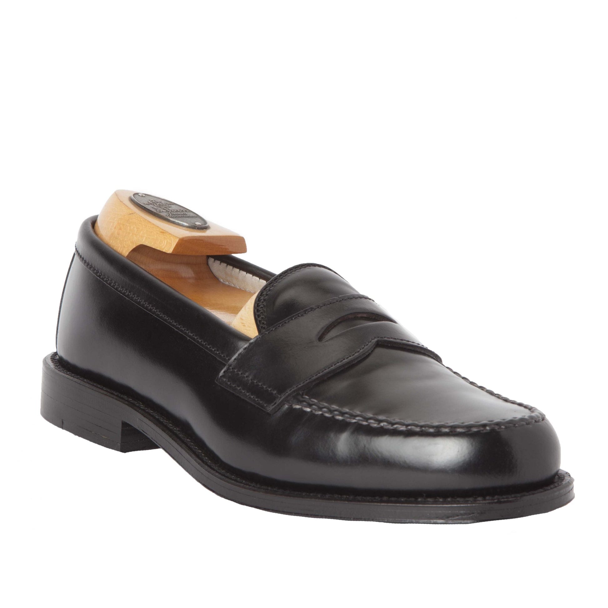 The Alden Madison 987 - Leisure Hand Sewn loafer is crafted in black Shell Cordovan, featuring a classic penny design, visible stitching, and a low heel. It includes a wooden shoe tree and has a durable Leather Outsole with a subtle right angle for added elegance.
