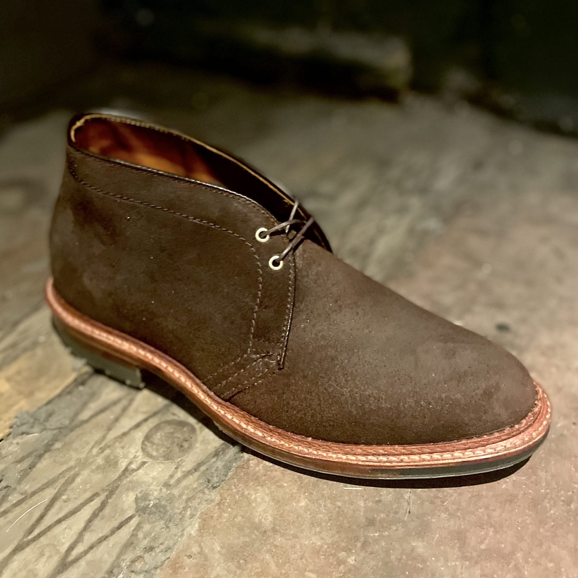 The Alden Madison D1717C Catskills Chukka Boot in Tobacco Reverse Chamois, featuring dark laces and a sturdy Commando sole, rests on a rustic wooden floor.