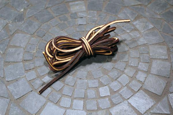 A bundle of Alden Madison Laces - Rawhide Laces in Brown/Tan tied together on a circular gray stone mosaic; perfect 74-inch laces that can be cut to size.
