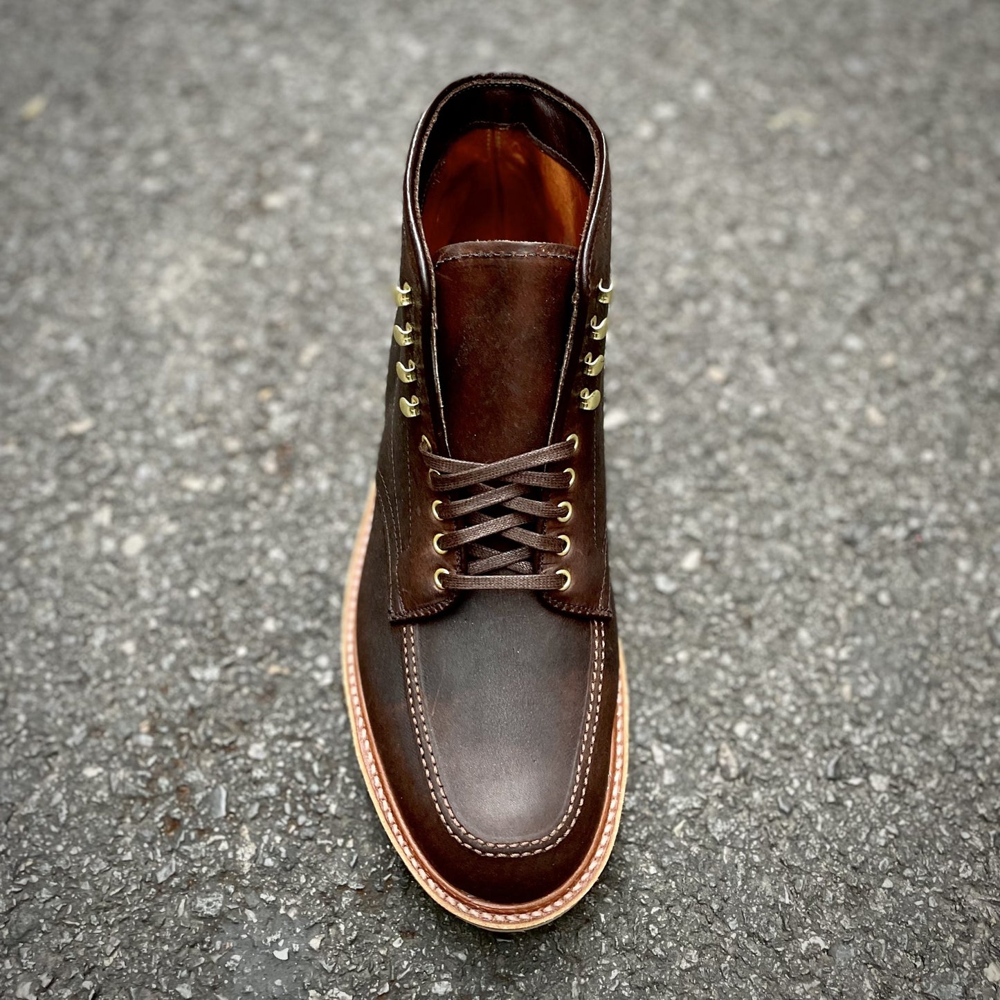 A top view of Alden Madisons D1926H - Porter Indy Boot in rich Kudu Leather with brass eyelets, dark brown laces, and a light brown sole, elegantly displayed on a textured gray surface.