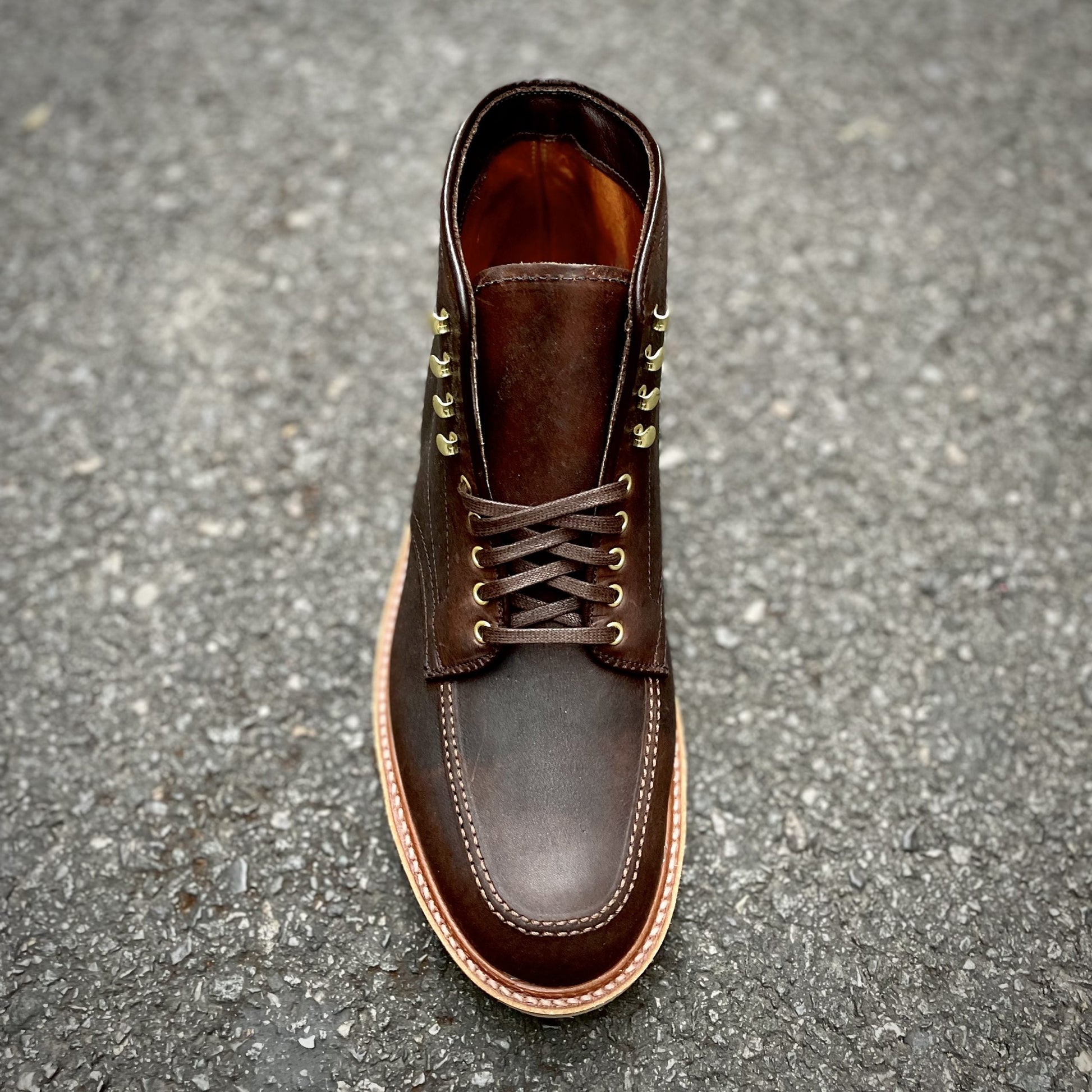 A top view of Alden Madisons D1926H - Porter Indy Boot in rich Kudu Leather with brass eyelets, dark brown laces, and a light brown sole, elegantly displayed on a textured gray surface.