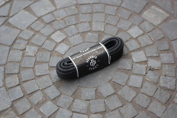 A bundle of black Alden Madison Laces - Round Boot Laces - 48 Inch with a labeled paper band lies on a circular stone tile pattern. The label reads Alden Madison and Round Boot Laces, 48 inches.