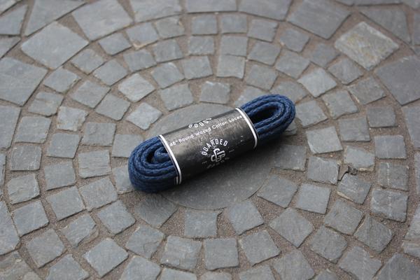 A pair of Alden Madison Laces - Round Boot Laces - 48 Inch, in dark blue, neatly coiled with a black label, rests on a circular mosaic stone pavement.