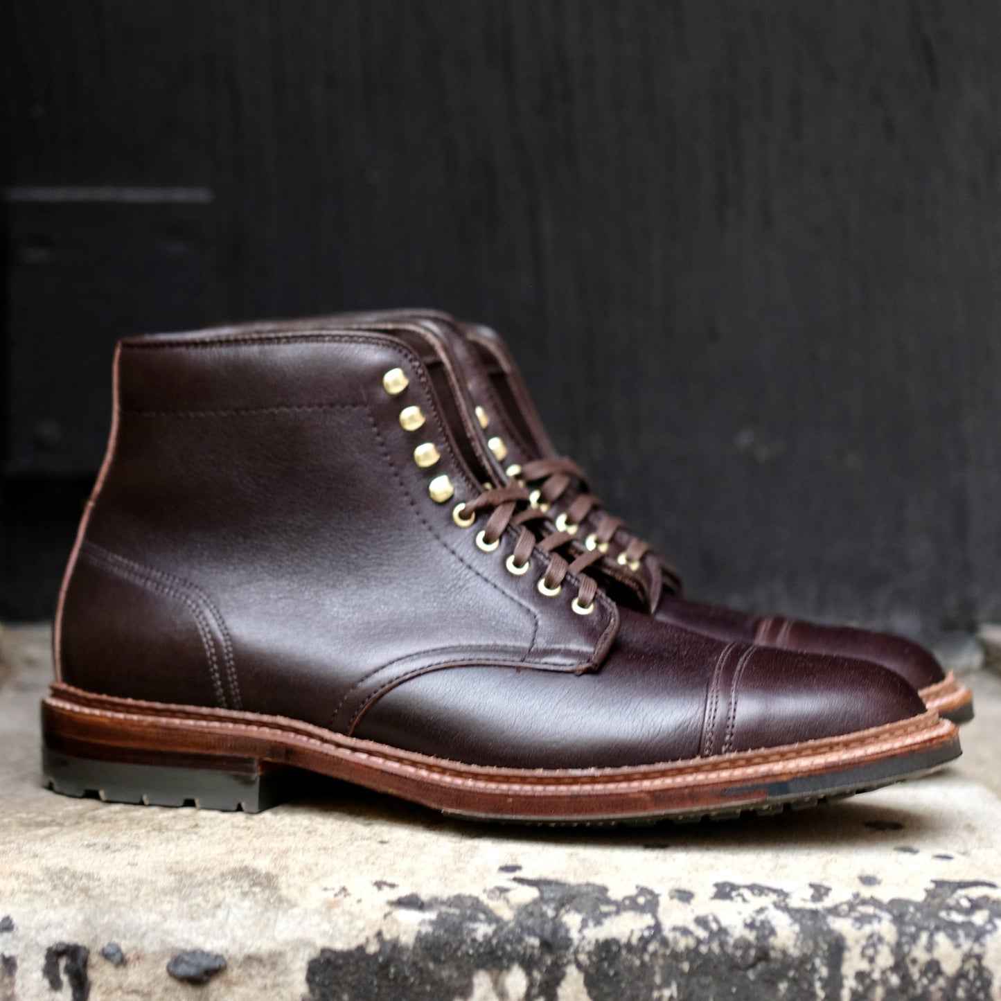 The Alden Madison D1808HC - Stitchup 2/2 Boot in Arabica Lux7 features dark brown Arabica Lux calfskin, gold eyelets, capped toe, contrast sole stitching, and a rugged Commando Sole, shown on stone against a black background.