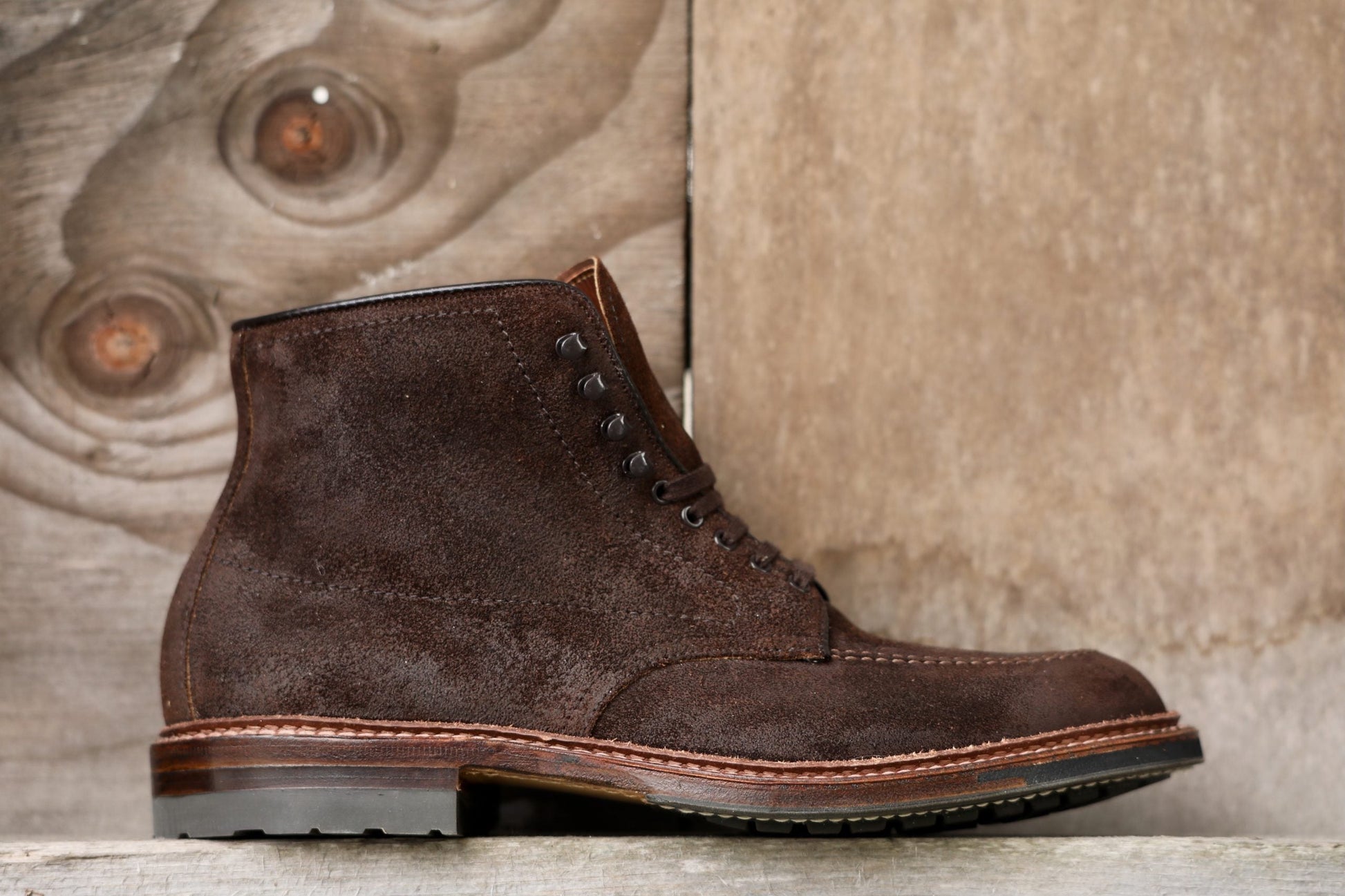 The Alden Madison 4015HC Indy Boot in Tobacco Reverse Chamois, featuring a commando sole and detailed stitching, is stylishly displayed against a wooden background, showcasing its rugged texture and sturdy appearance.