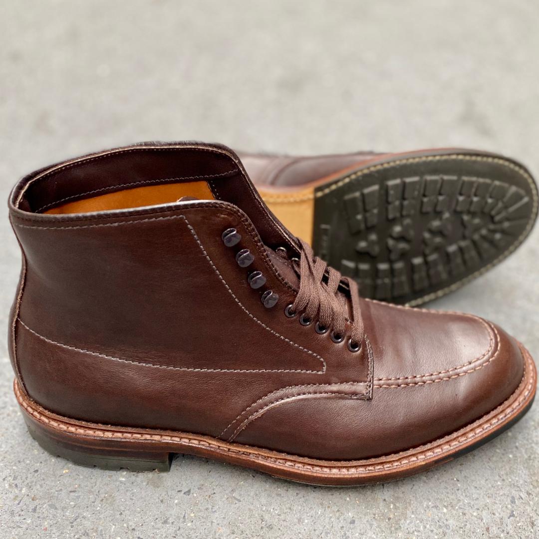 The Alden Madison 4012HC Indy Boot in Brown Rusticalf features eyelet hooks, visible stitching, and sturdy 360 Commando Soles. One upright and one side-laid boot are displayed on a light grey surface.