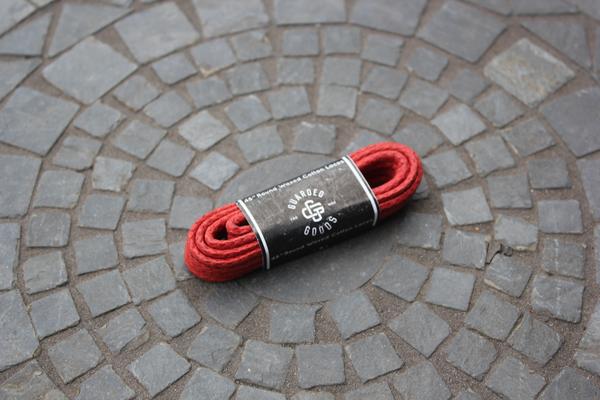 A pair of 48-inch Round Boot Laces from Alden Madison, wrapped in a black and white label, lies on a circular mosaic stone pavement.