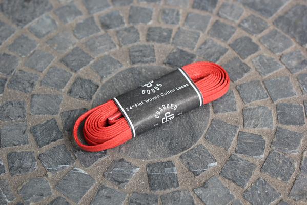 A bundle of Alden Madisons Flat Boot Laces, 54 inches and adorned with a black label, rests on a textured stone pavement. The display forms concentric circles beneath the laces.
