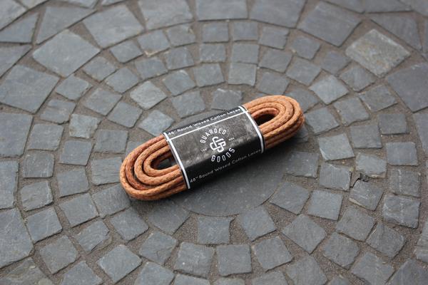 A 48-inch round boot lace by Alden Madison, coiled with a black and white label, rests on circular mosaic stone pavement.